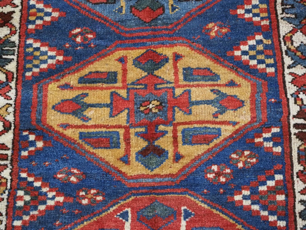 An antique hand-knotted Caucasian wool runner rug featuring a sequence of geometric diamond medallions on an indigo blue field surrounded by patterned borders. View XV