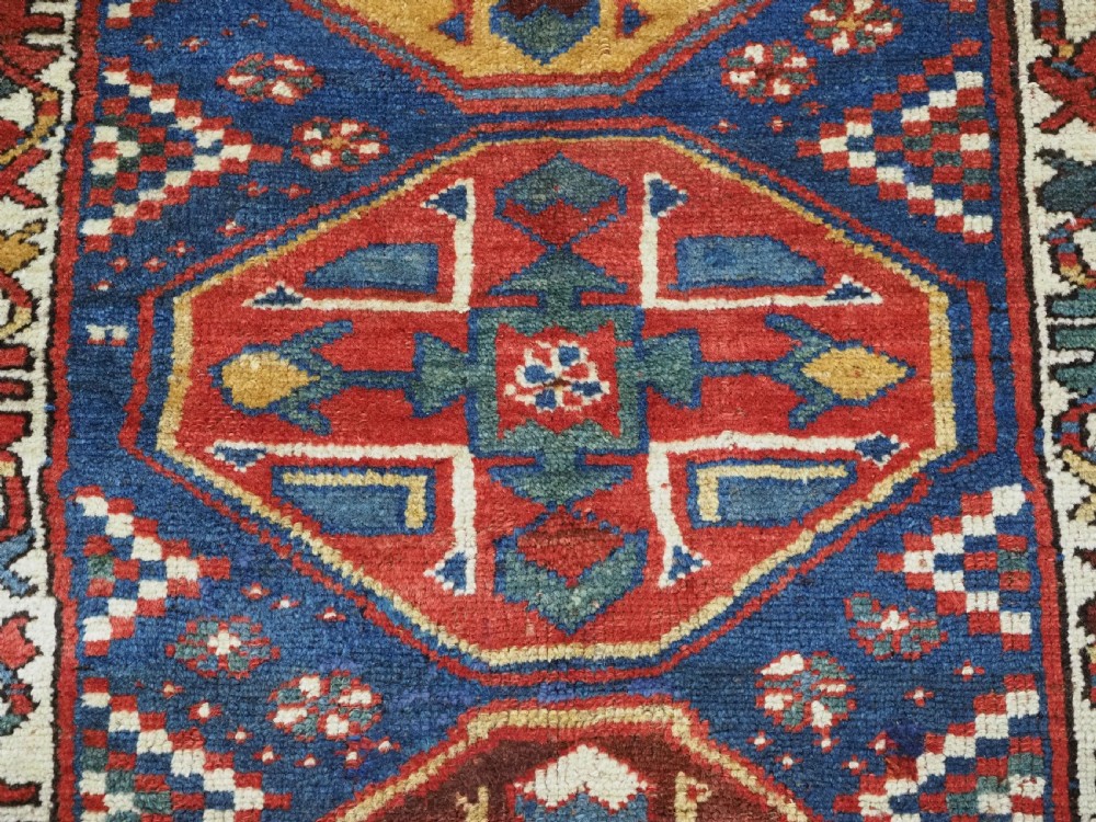An antique hand-knotted Caucasian wool runner rug featuring a sequence of geometric diamond medallions on an indigo blue field surrounded by patterned borders. View XIX
