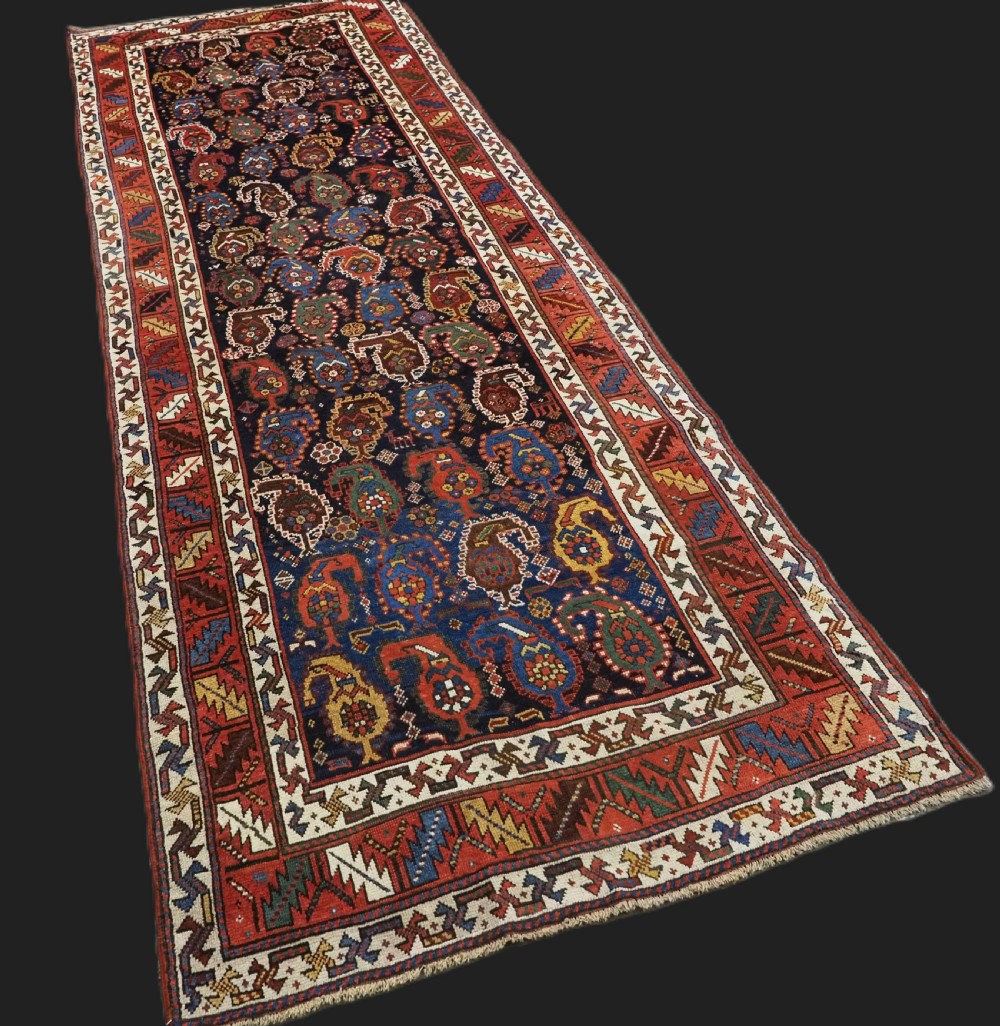 An antique Caucasian Gendje Kazak wool runner rug featuring repeating colourful boteh motifs on a dark navy field framed by geometric red and white borders. View II
