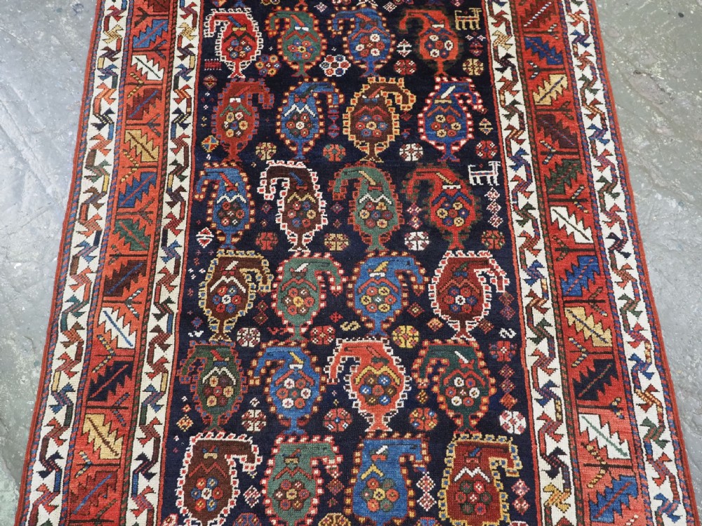 An antique Caucasian Gendje Kazak wool runner rug featuring repeating colourful boteh motifs on a dark navy field framed by geometric red and white borders. View V
