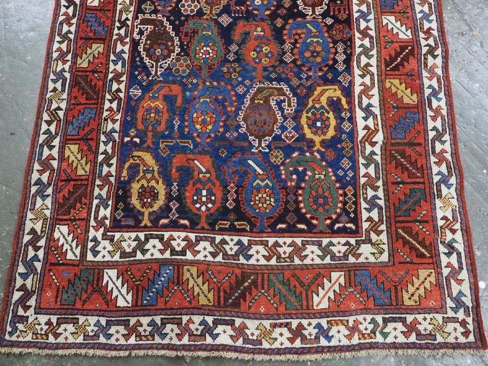 An antique Caucasian Gendje Kazak wool runner rug featuring repeating colourful boteh motifs on a dark navy field framed by geometric red and white borders. View VII