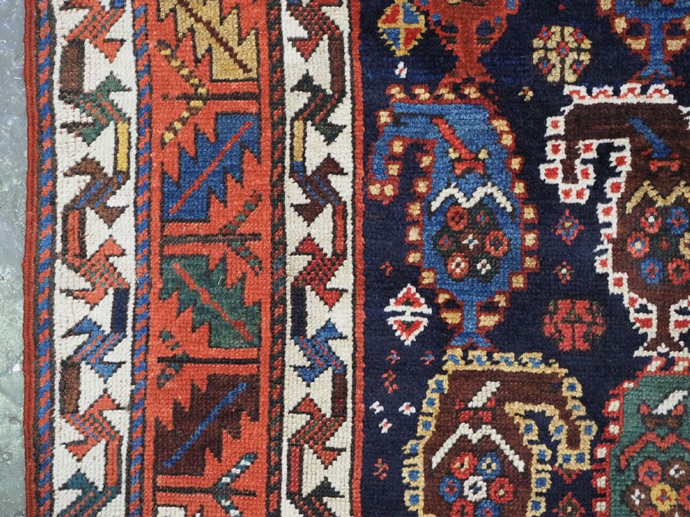 An antique Caucasian Gendje Kazak wool runner rug featuring repeating colourful boteh motifs on a dark navy field framed by geometric red and white borders. View IX