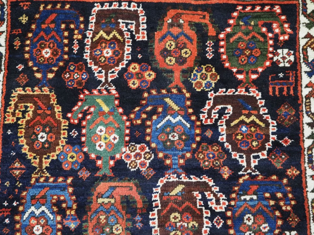 An antique Caucasian Gendje Kazak wool runner rug featuring repeating colourful boteh motifs on a dark navy field framed by geometric red and white borders. View X