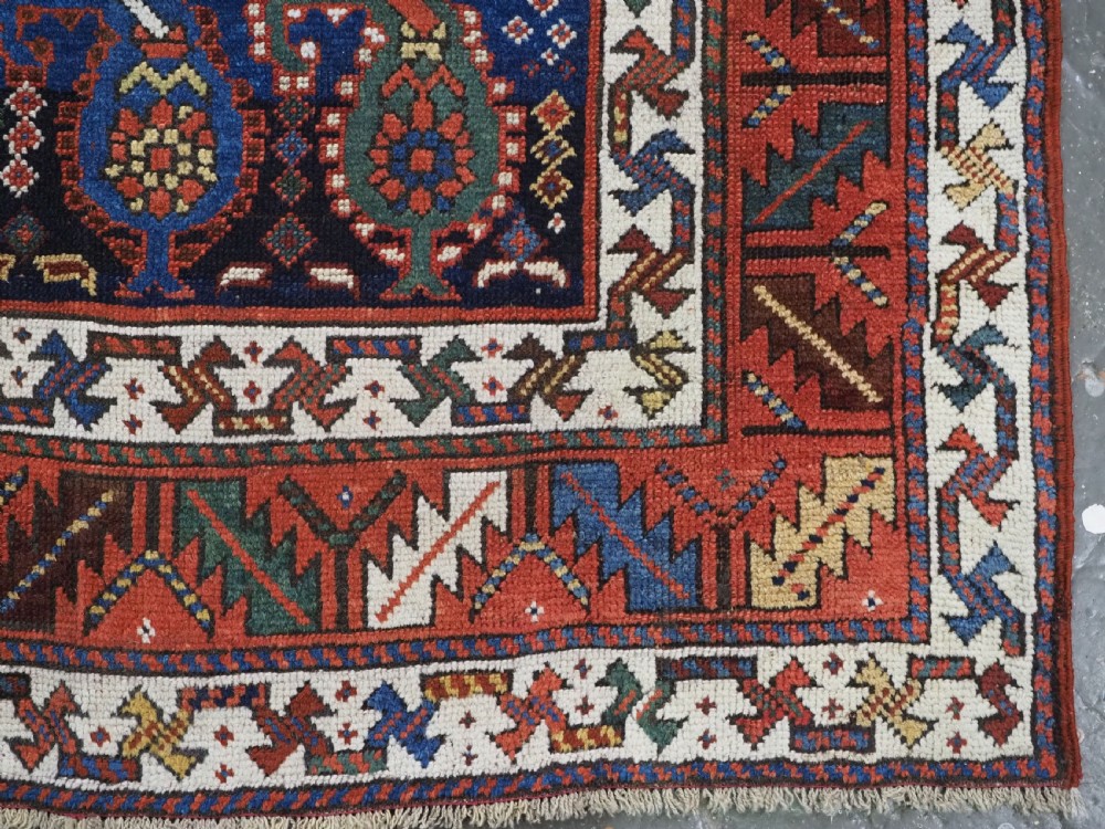 An antique Caucasian Gendje Kazak wool runner rug featuring repeating colourful boteh motifs on a dark navy field framed by geometric red and white borders. View XVI