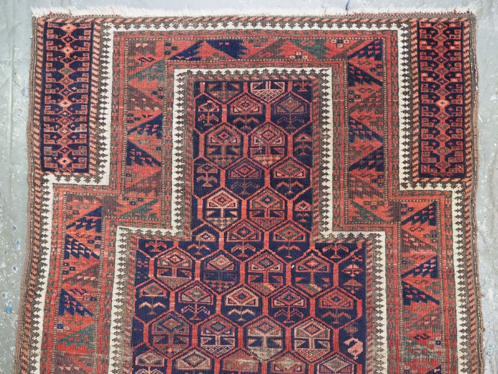 A hand-knotted wool prayer rug with a stepped mihrab niche, repeating geometric tree motifs, and a dark indigo blue and terracotta red palette. View III