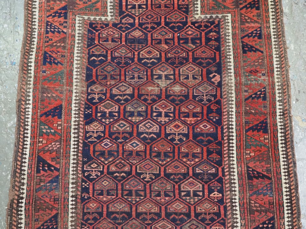 A hand-knotted wool prayer rug with a stepped mihrab niche, repeating geometric tree motifs, and a dark indigo blue and terracotta red palette. View V