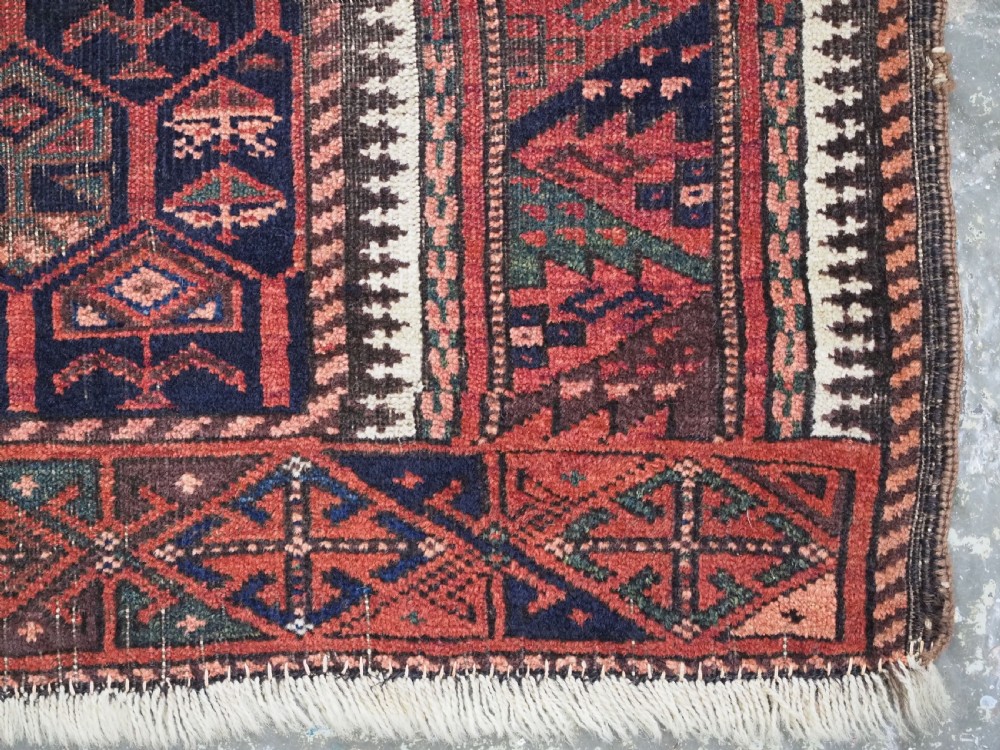 A hand-knotted wool prayer rug with a stepped mihrab niche, repeating geometric tree motifs, and a dark indigo blue and terracotta red palette. View VII
