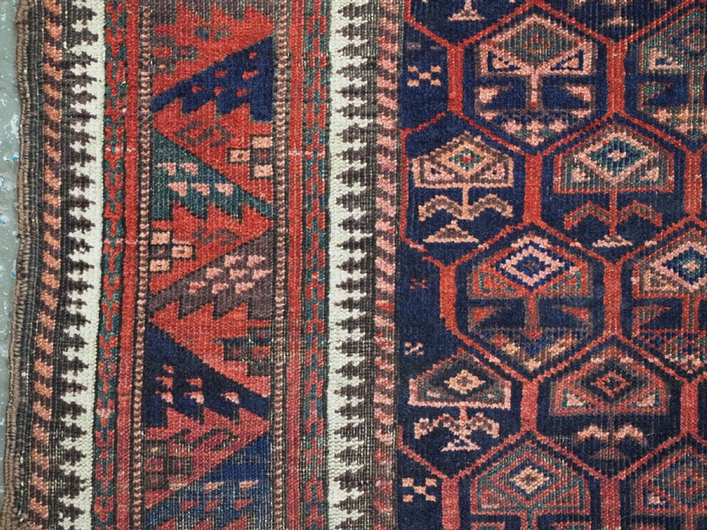 A hand-knotted wool prayer rug with a stepped mihrab niche, repeating geometric tree motifs, and a dark indigo blue and terracotta red palette. View VIII