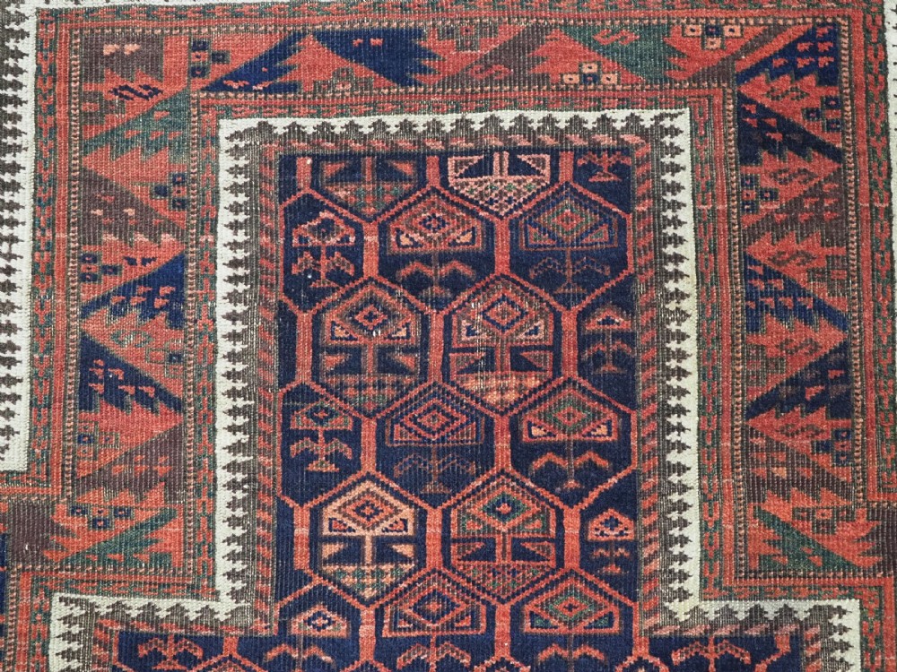 A hand-knotted wool prayer rug with a stepped mihrab niche, repeating geometric tree motifs, and a dark indigo blue and terracotta red palette. View IX