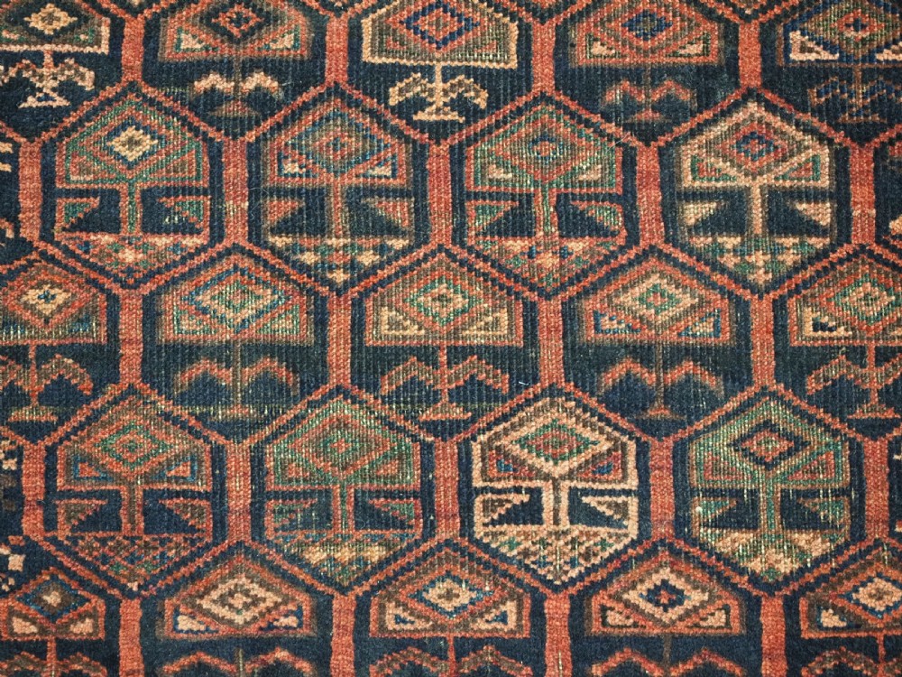 A hand-knotted wool prayer rug with a stepped mihrab niche, repeating geometric tree motifs, and a dark indigo blue and terracotta red palette. View X