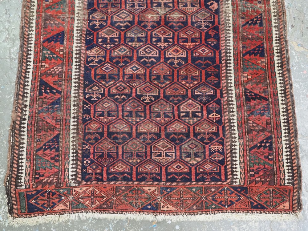 A hand-knotted wool prayer rug with a stepped mihrab niche, repeating geometric tree motifs, and a dark indigo blue and terracotta red palette. View XI