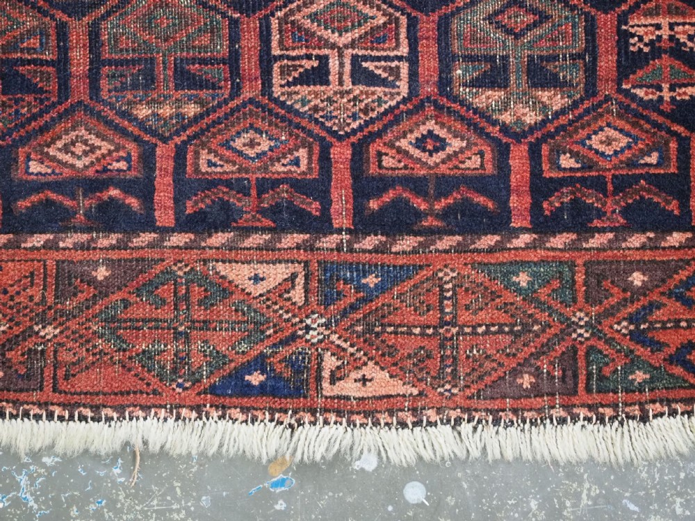 A hand-knotted wool prayer rug with a stepped mihrab niche, repeating geometric tree motifs, and a dark indigo blue and terracotta red palette. View XIV