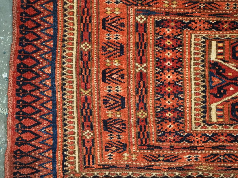 An elongated antique Turkmen torba textile displaying geometric diamond medallion motifs in deep red, dark navy, and cream wool with fringed bottom edge. View IV