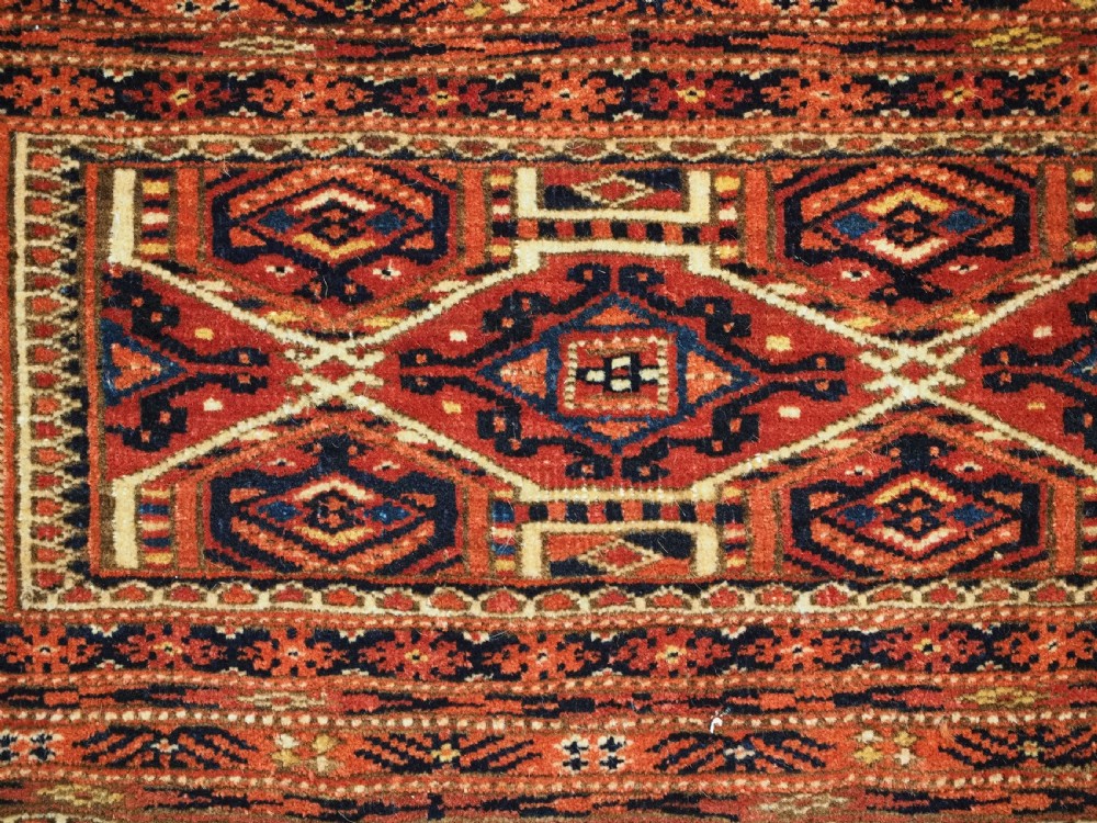 An elongated antique Turkmen torba textile displaying geometric diamond medallion motifs in deep red, dark navy, and cream wool with fringed bottom edge. View VI