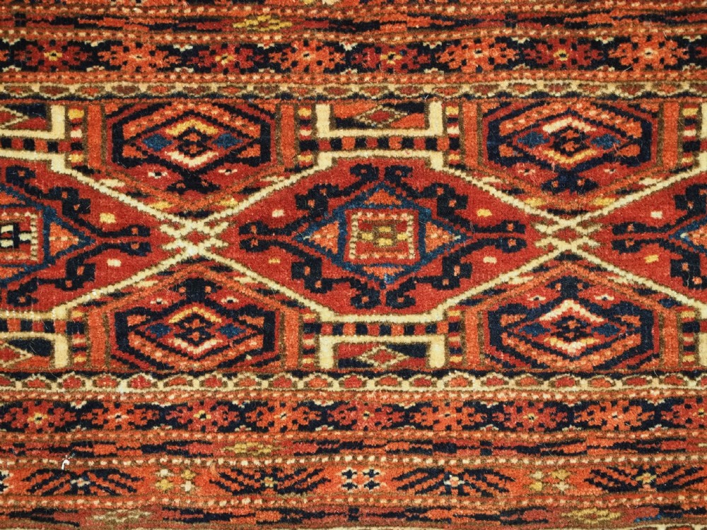 An elongated antique Turkmen torba textile displaying geometric diamond medallion motifs in deep red, dark navy, and cream wool with fringed bottom edge. View VII