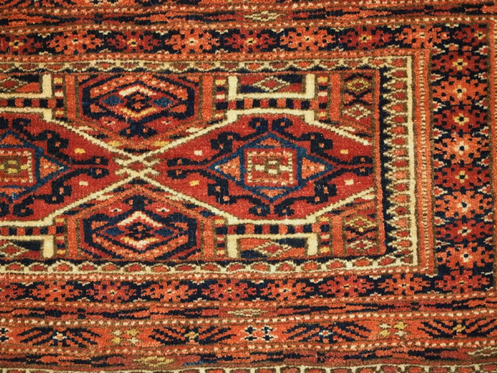 An elongated antique Turkmen torba textile displaying geometric diamond medallion motifs in deep red, dark navy, and cream wool with fringed bottom edge. View VIII