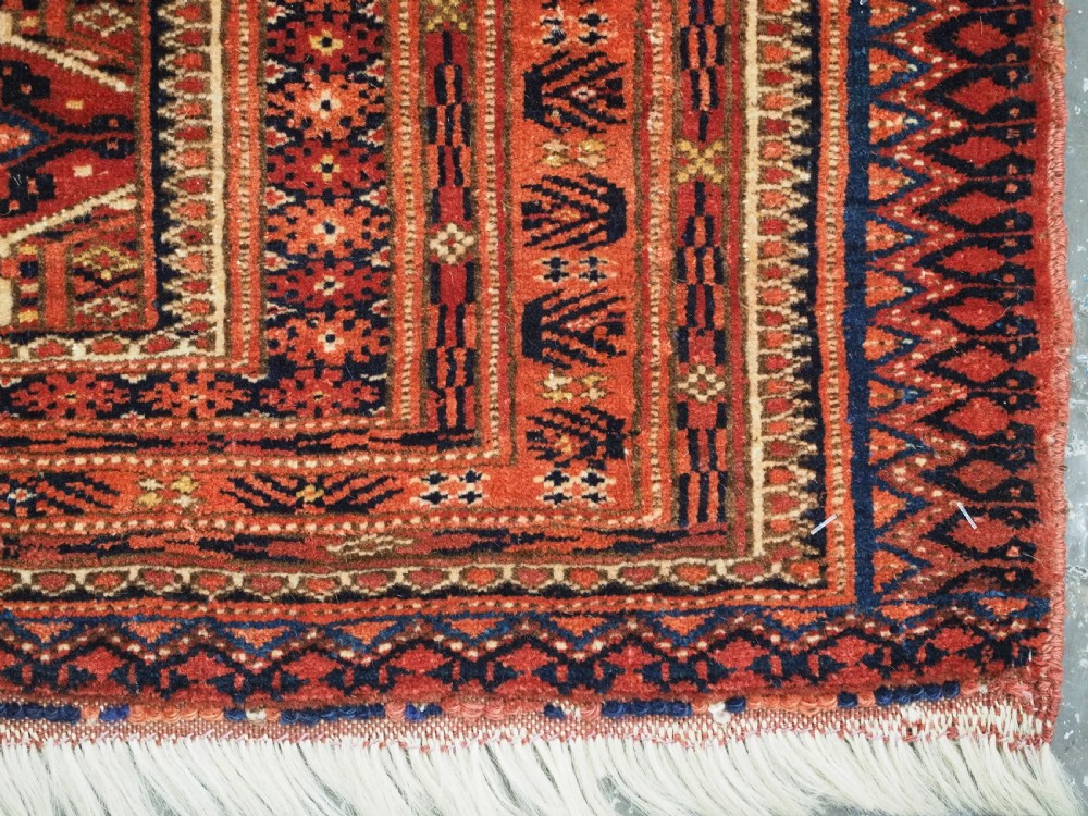 An elongated antique Turkmen torba textile displaying geometric diamond medallion motifs in deep red, dark navy, and cream wool with fringed bottom edge. View IX