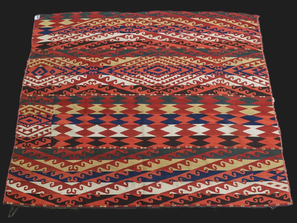 A rectangular handwoven flatweave kilim panel featuring horizontal bands of geometric diamonds, zig-zags, and latch-hook motifs in red, cream, navy blue, and ochre wool.