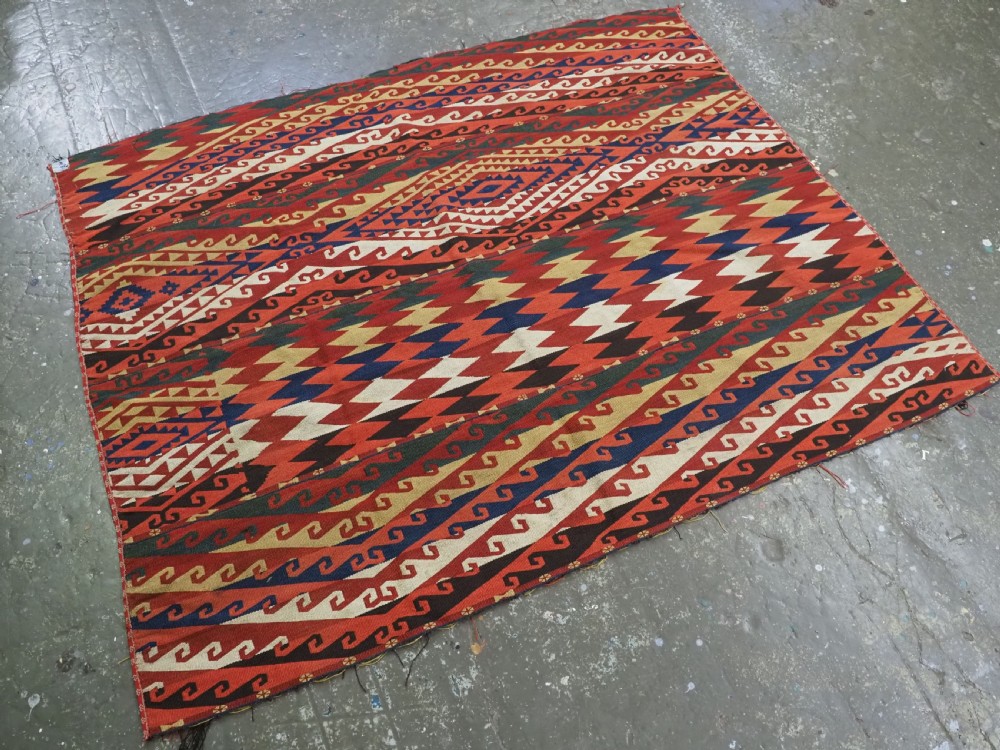 A rectangular handwoven flatweave kilim panel featuring horizontal bands of geometric diamonds, zig-zags, and latch-hook motifs in red, cream, navy blue, and ochre wool. View II