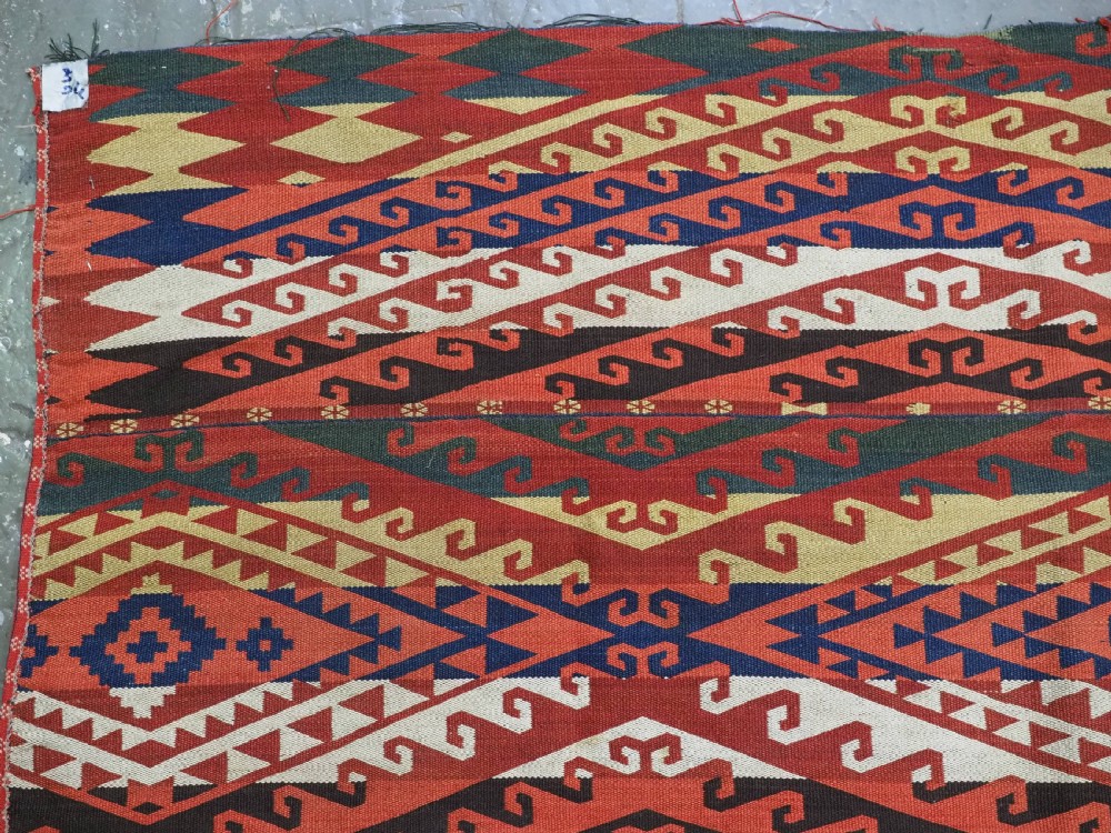 A rectangular handwoven flatweave kilim panel featuring horizontal bands of geometric diamonds, zig-zags, and latch-hook motifs in red, cream, navy blue, and ochre wool. View III