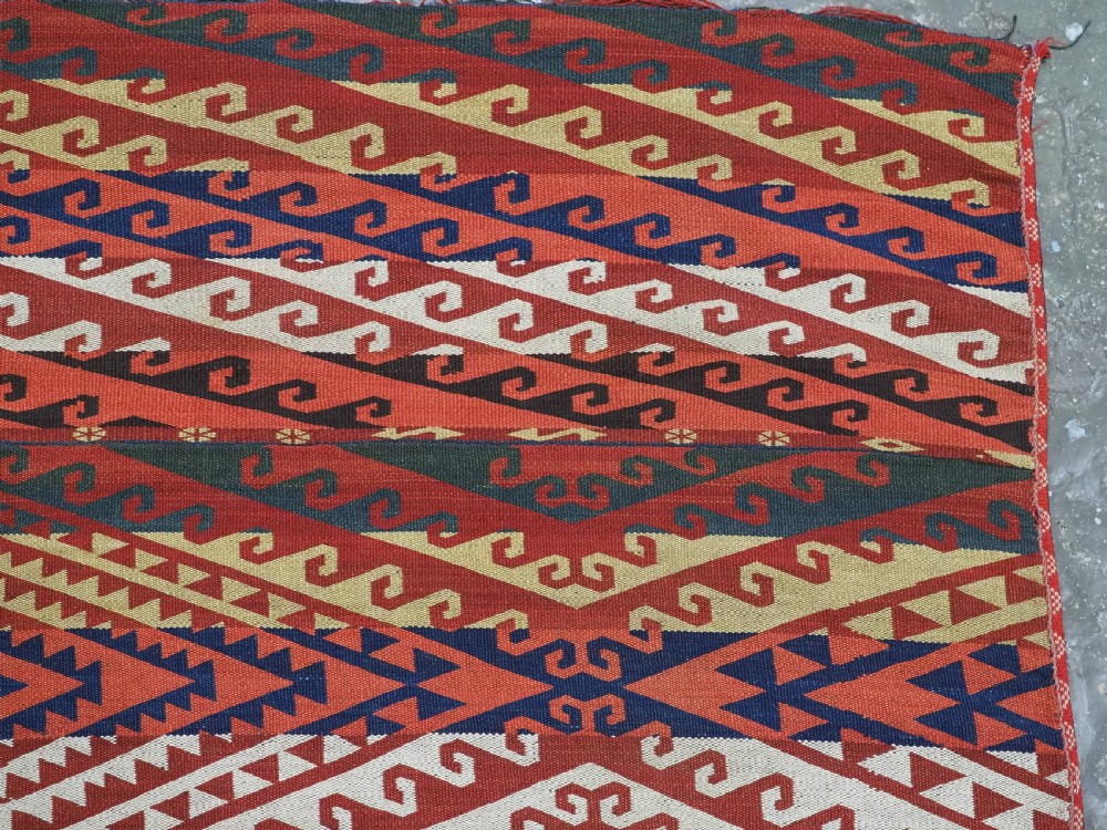 A rectangular handwoven flatweave kilim panel featuring horizontal bands of geometric diamonds, zig-zags, and latch-hook motifs in red, cream, navy blue, and ochre wool. View VI