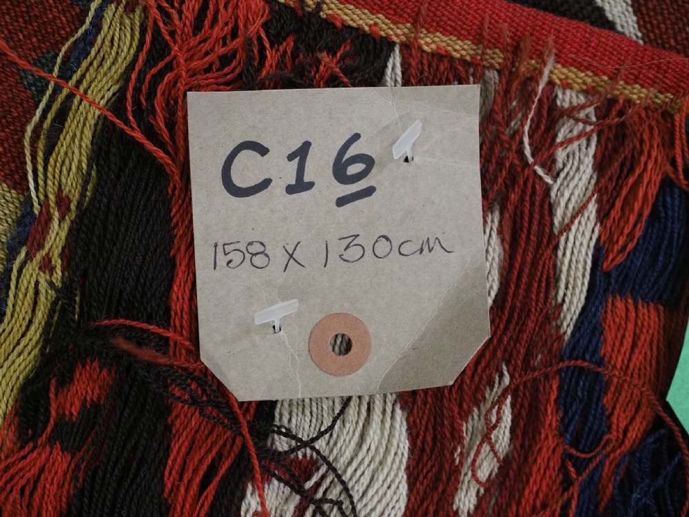 A rectangular handwoven flatweave kilim panel featuring horizontal bands of geometric diamonds, zig-zags, and latch-hook motifs in red, cream, navy blue, and ochre wool. View VII