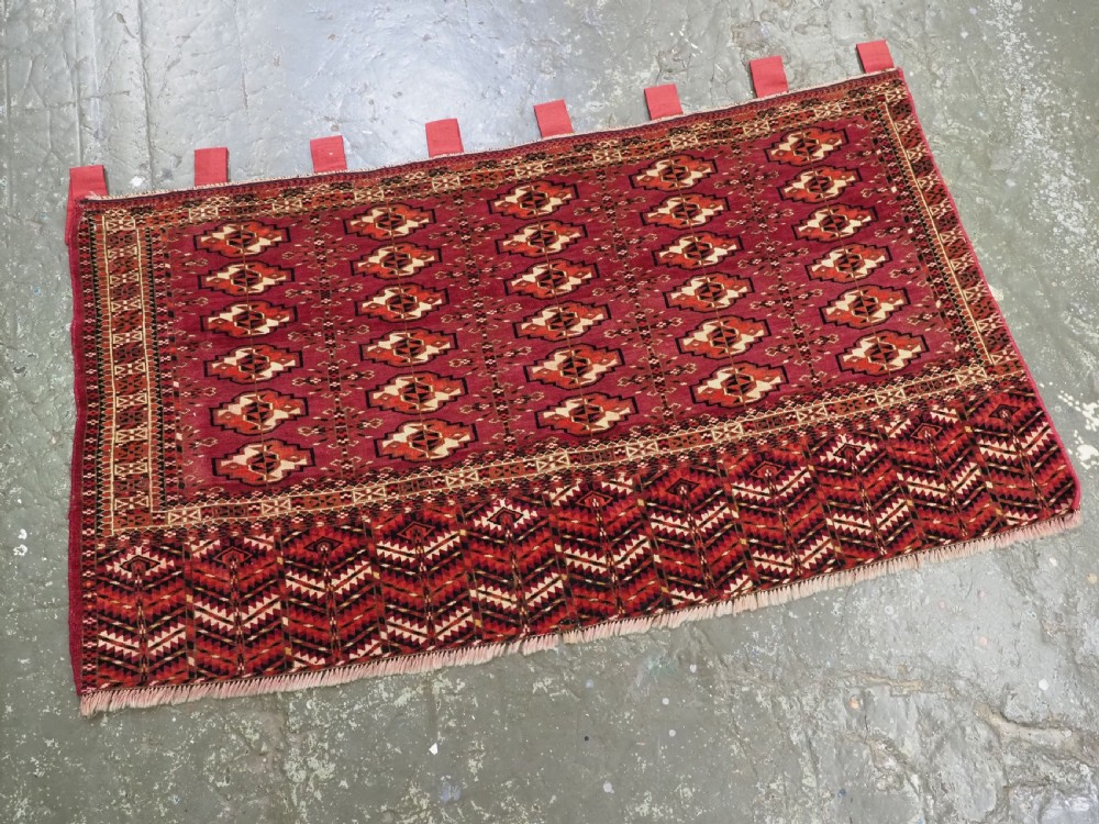 A woven deep red antique Turkmen chuval face textile featuring 30 repeating octagonal guls, an ornate geometric lower border, and fabric hanging loops along the top edge. View II