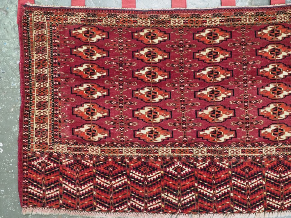 A woven deep red antique Turkmen chuval face textile featuring 30 repeating octagonal guls, an ornate geometric lower border, and fabric hanging loops along the top edge. View III