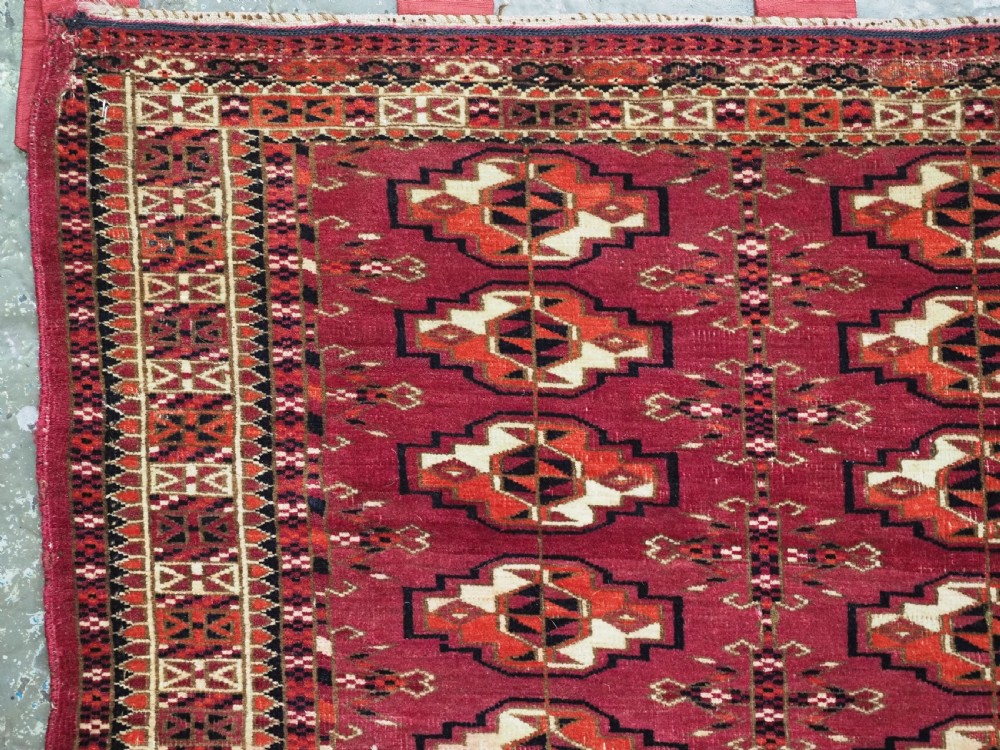 A woven deep red antique Turkmen chuval face textile featuring 30 repeating octagonal guls, an ornate geometric lower border, and fabric hanging loops along the top edge. View V
