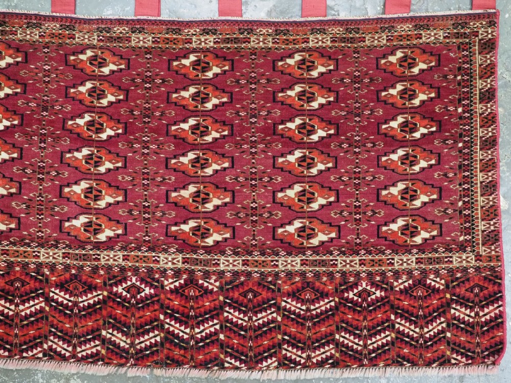 A woven deep red antique Turkmen chuval face textile featuring 30 repeating octagonal guls, an ornate geometric lower border, and fabric hanging loops along the top edge. View VI