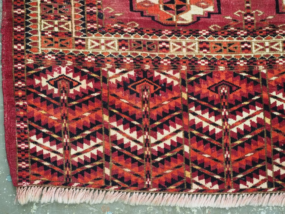 A woven deep red antique Turkmen chuval face textile featuring 30 repeating octagonal guls, an ornate geometric lower border, and fabric hanging loops along the top edge. View VII