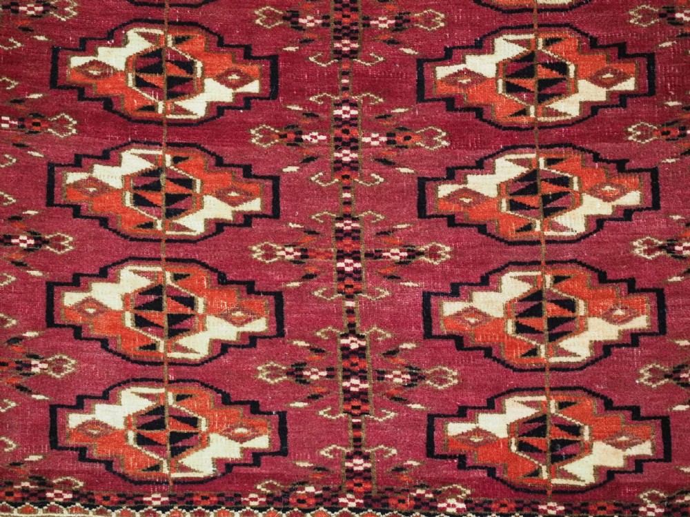 A woven deep red antique Turkmen chuval face textile featuring 30 repeating octagonal guls, an ornate geometric lower border, and fabric hanging loops along the top edge. View VIII