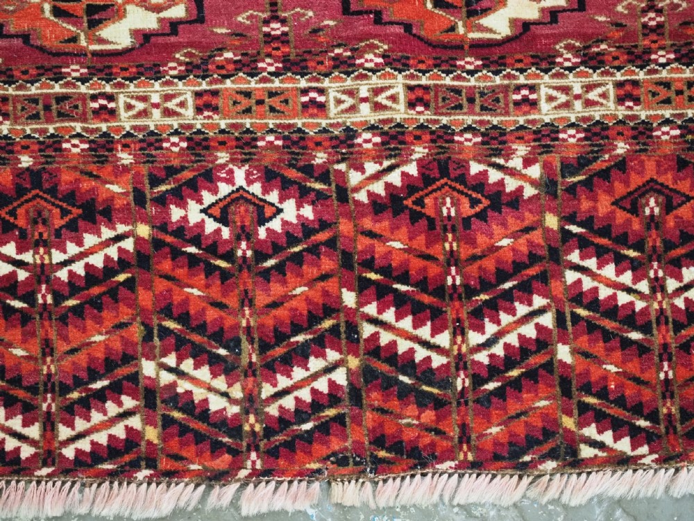 A woven deep red antique Turkmen chuval face textile featuring 30 repeating octagonal guls, an ornate geometric lower border, and fabric hanging loops along the top edge. View IX