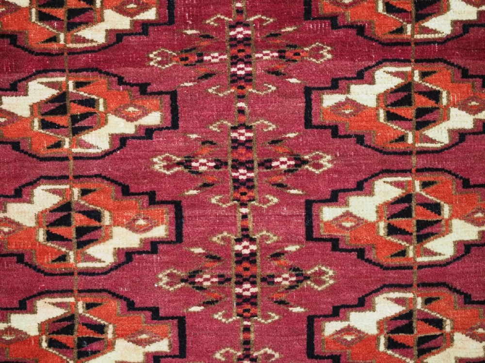 A woven deep red antique Turkmen chuval face textile featuring 30 repeating octagonal guls, an ornate geometric lower border, and fabric hanging loops along the top edge. View X