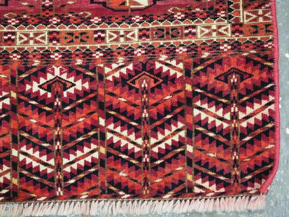 A woven deep red antique Turkmen chuval face textile featuring 30 repeating octagonal guls, an ornate geometric lower border, and fabric hanging loops along the top edge. View XI