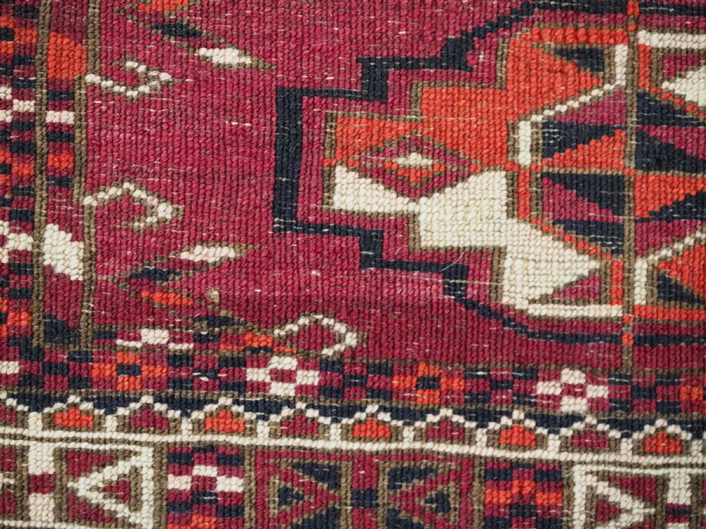 A woven deep red antique Turkmen chuval face textile featuring 30 repeating octagonal guls, an ornate geometric lower border, and fabric hanging loops along the top edge. View XII