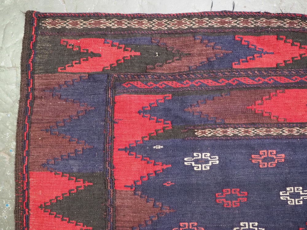 A rectangular antique Baluch sofreh flatweave textile featuring an indigo blue centre with small geometric motifs framed by serrated red and dark blue borders. View II
