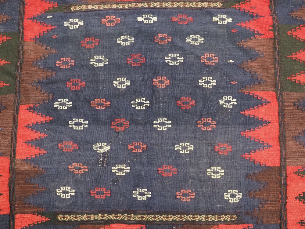 A rectangular antique Baluch sofreh flatweave textile featuring an indigo blue centre with small geometric motifs framed by serrated red and dark blue borders. View III