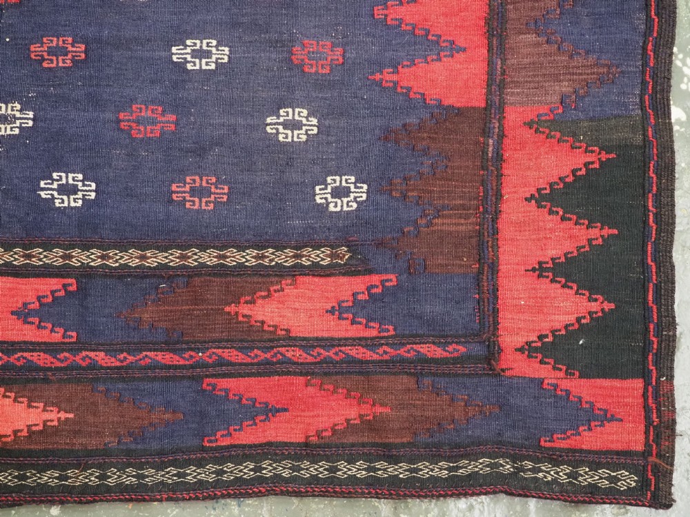A rectangular antique Baluch sofreh flatweave textile featuring an indigo blue centre with small geometric motifs framed by serrated red and dark blue borders. View V