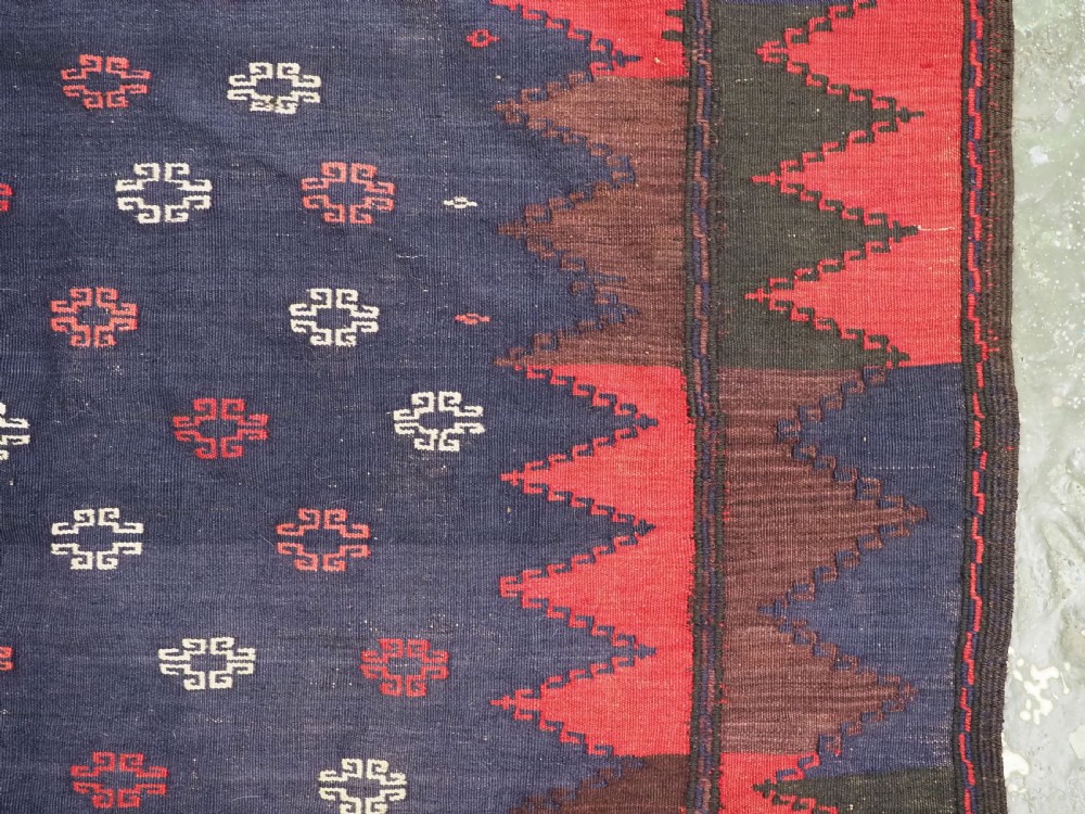 A rectangular antique Baluch sofreh flatweave textile featuring an indigo blue centre with small geometric motifs framed by serrated red and dark blue borders. View VI