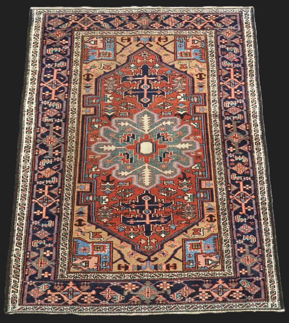 An antique hand-knotted Persian Heriz rug featuring a central starburst medallion in teal, terracotta, and cream on a patterned ground with a multi-band geometric border.