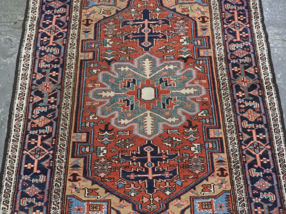 An antique hand-knotted Persian Heriz rug featuring a central starburst medallion in teal, terracotta, and cream on a patterned ground with a multi-band geometric border. View IV