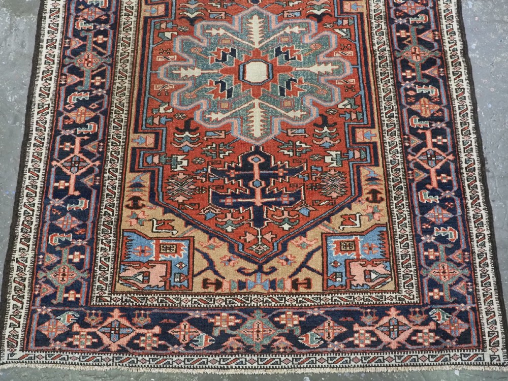 An antique hand-knotted Persian Heriz rug featuring a central starburst medallion in teal, terracotta, and cream on a patterned ground with a multi-band geometric border. View V