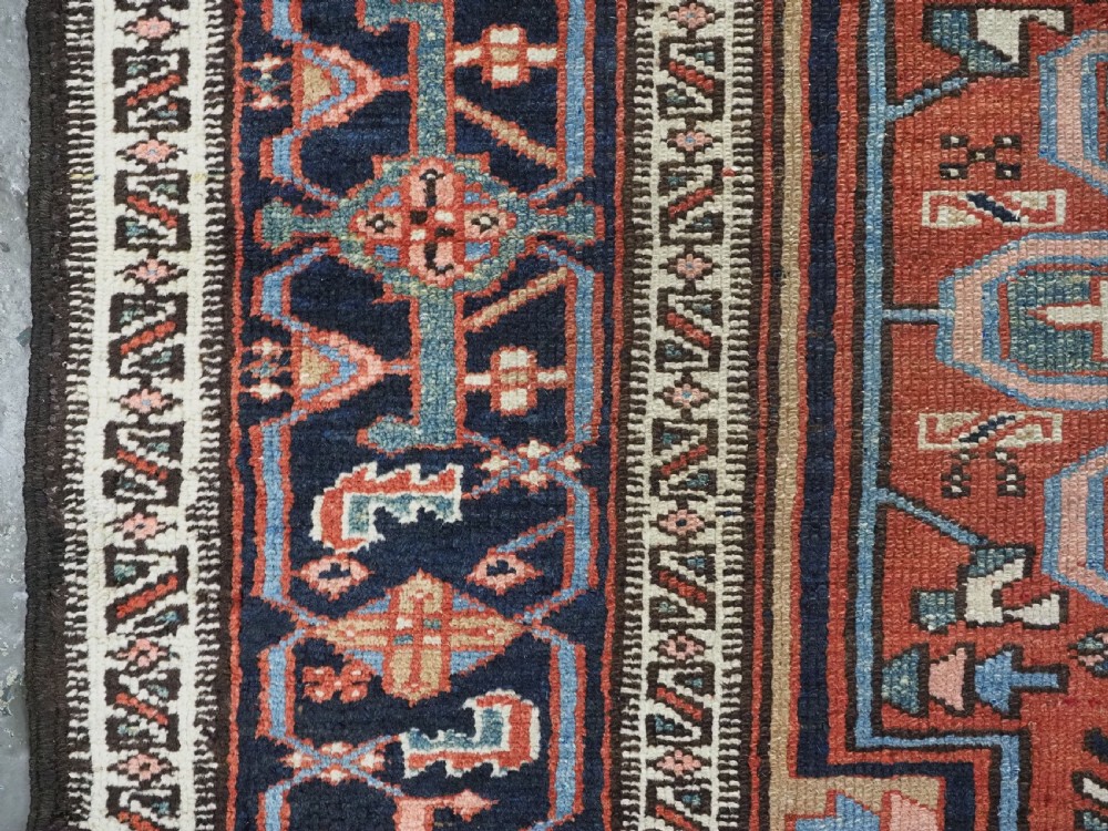 An antique hand-knotted Persian Heriz rug featuring a central starburst medallion in teal, terracotta, and cream on a patterned ground with a multi-band geometric border. View VII