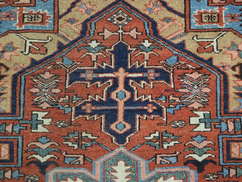 An antique hand-knotted Persian Heriz rug featuring a central starburst medallion in teal, terracotta, and cream on a patterned ground with a multi-band geometric border. View X