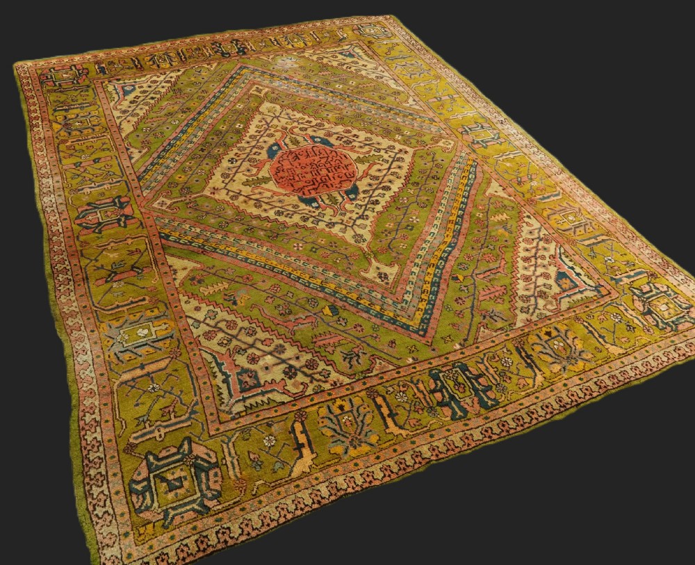 An antique Turkish Oushak wool carpet featuring an olive green field with a central cream and coral diamond medallion surrounded by detailed geometric borders.