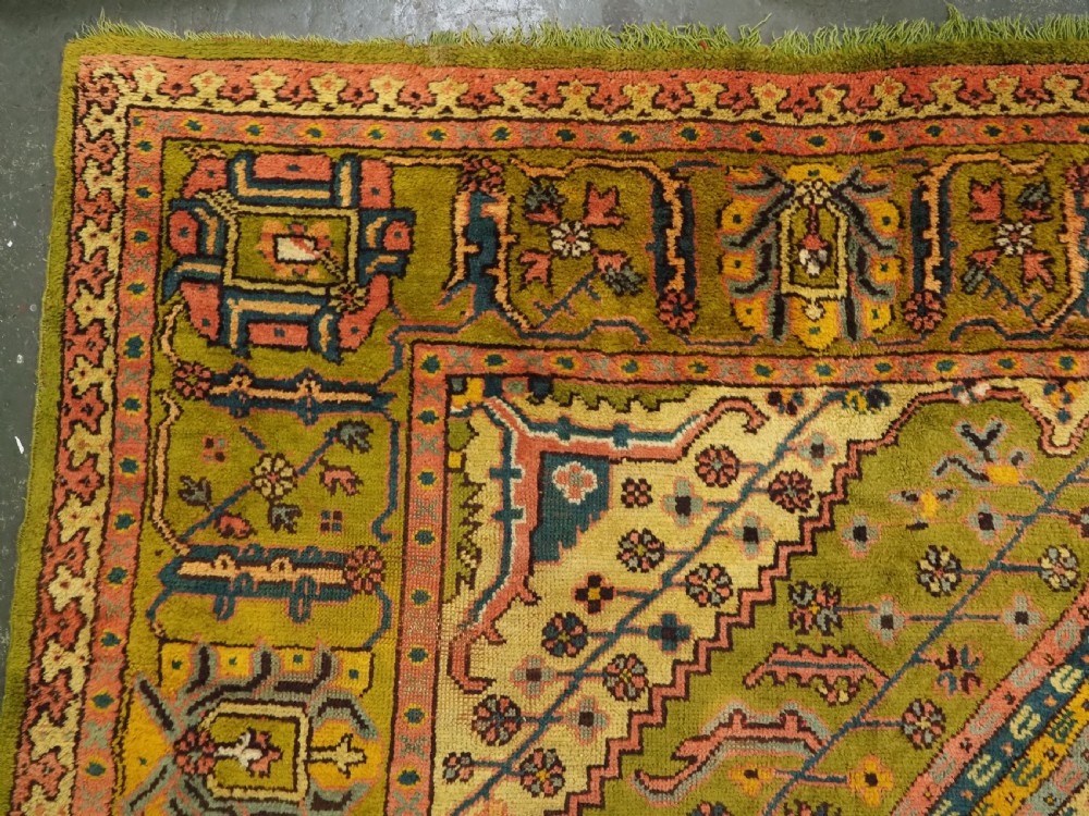 An antique Turkish Oushak wool carpet featuring an olive green field with a central cream and coral diamond medallion surrounded by detailed geometric borders. View IV