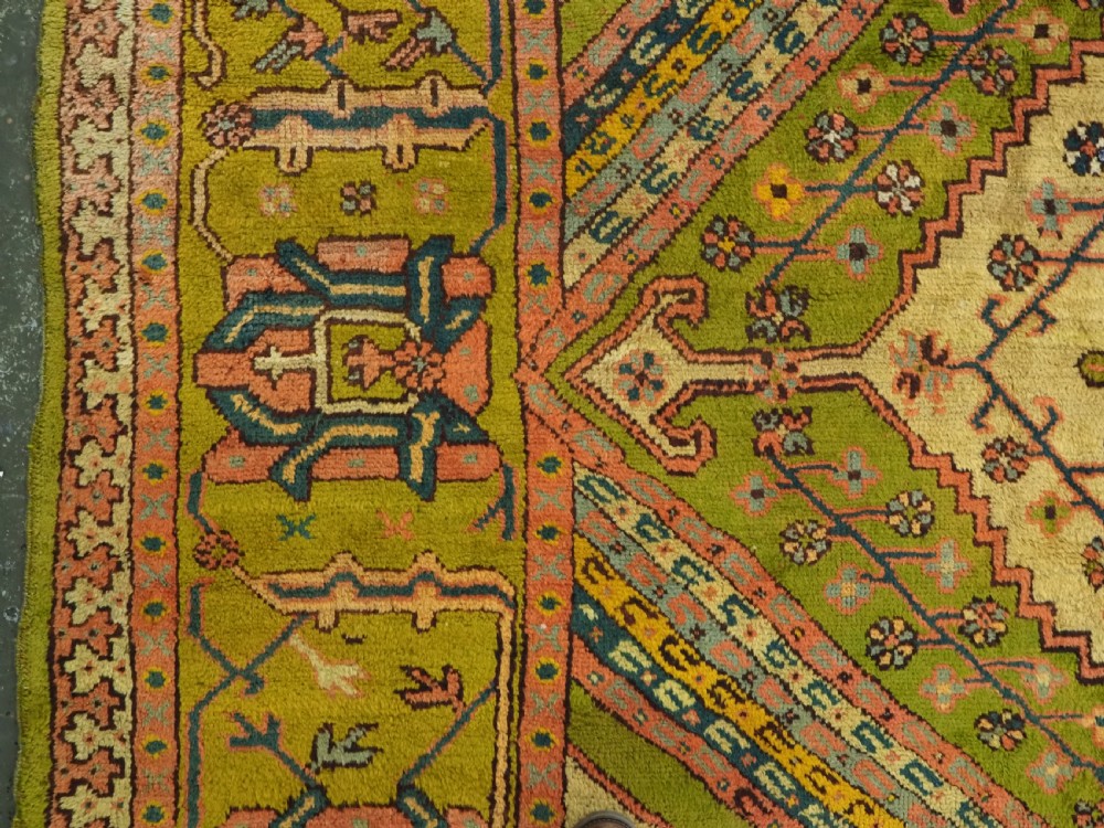 An antique Turkish Oushak wool carpet featuring an olive green field with a central cream and coral diamond medallion surrounded by detailed geometric borders. View V