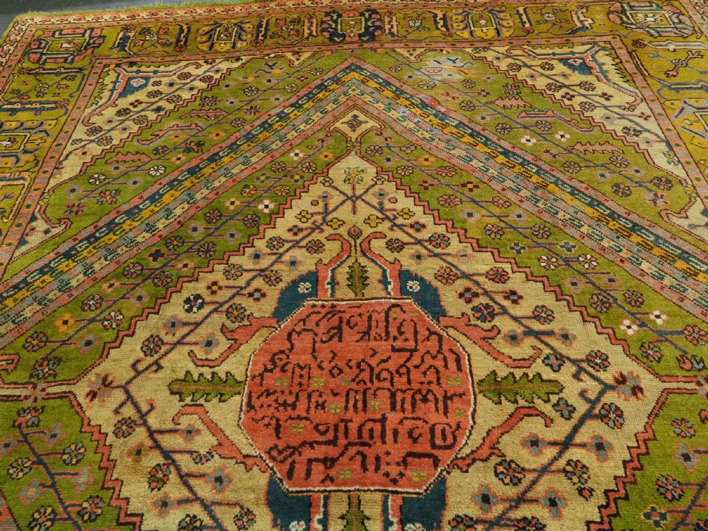 An antique Turkish Oushak wool carpet featuring an olive green field with a central cream and coral diamond medallion surrounded by detailed geometric borders. View VI