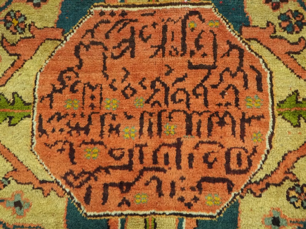 An antique Turkish Oushak wool carpet featuring an olive green field with a central cream and coral diamond medallion surrounded by detailed geometric borders. View X